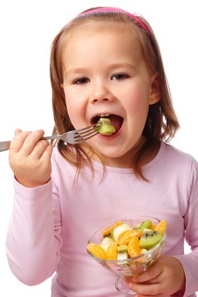 Five-year old girl eating kiwi.